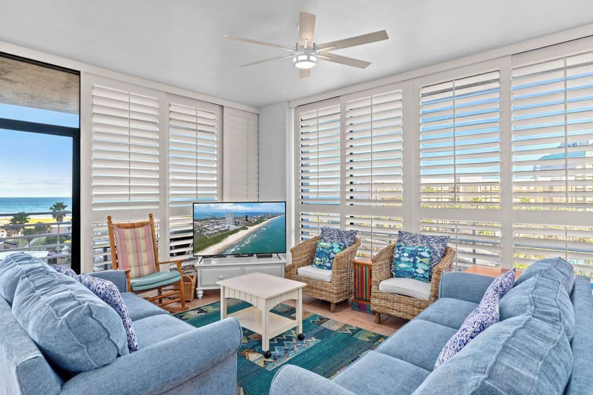 A spacious living room with a large TV, comfortable seating, and a view of the ocean.
