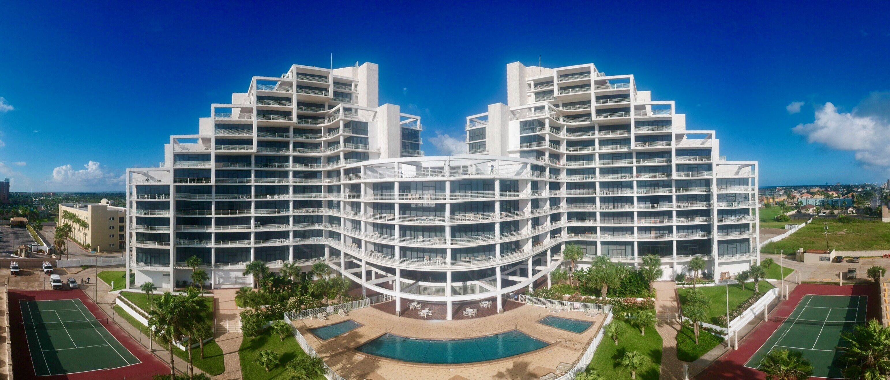 A modern hotel with multiple balconies, a central courtyard with a pool, and tennis courts.