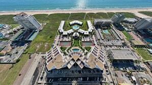 An aerial view of a coastal hotel with multiple buildings, a beach, and a large parking area. - Sunchase IV by South Padre Resort Rental (South Padre Island)