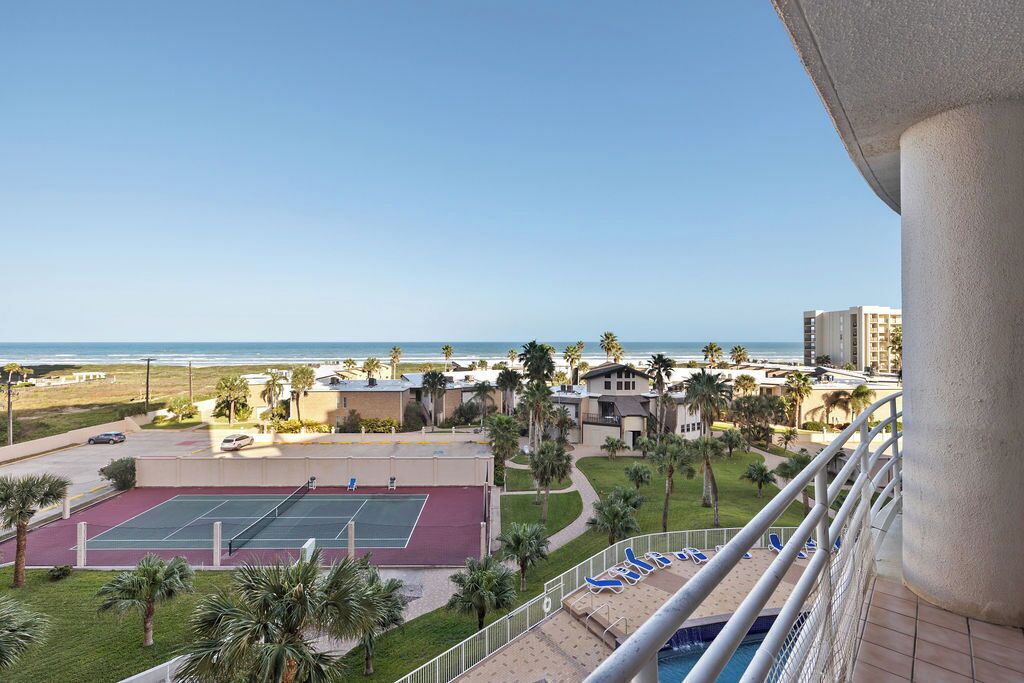 Quadra de tênis, piscina e vista para a praia a partir de uma varanda.