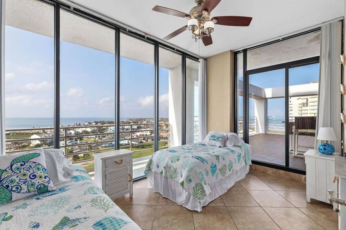 A bedroom with a large window, a ceiling fan, and a view of the city.