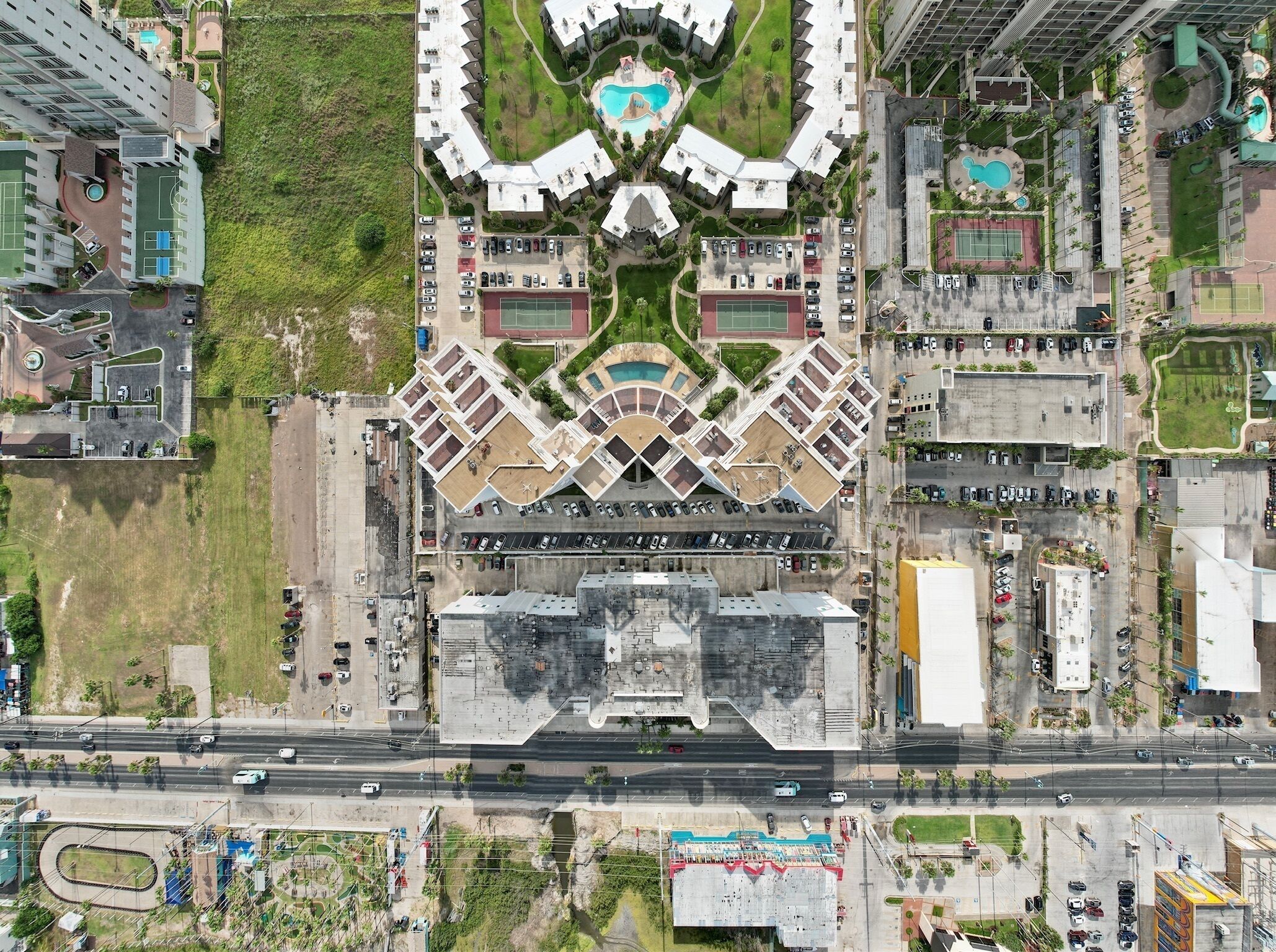Vue aérienne d’un hôtel moderne doté d’une cour intérieure, de plusieurs niveaux de stationnement et d’un espace verdoyant environnant.