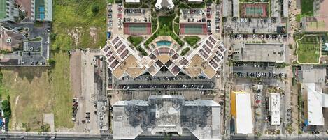 Vista aérea de un hotel moderno con un patio central, varios niveles de estacionamiento y zonas verdes circundantes.