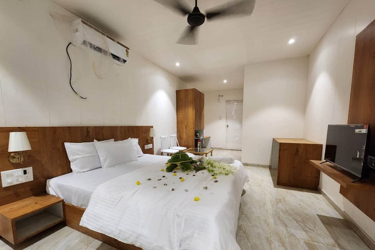A hotel room with a large bed, a wooden headboard, a ceiling fan, a TV, and a small table with a chair.