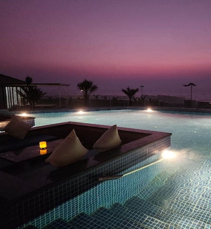 An infinity pool with a view of the ocean at dusk, equipped with lounge chairs and a small table with a candle.
