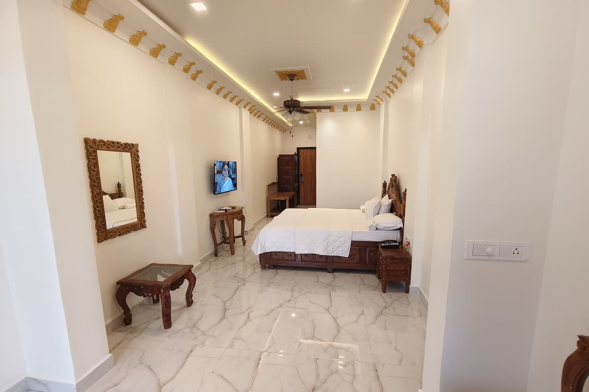 A bedroom with a bed, a TV, a wooden side table, and a marble floor.