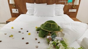 A neatly made bed with white linens, a green plush turtle, scattered seashells, and a small basket with flowers. - Casa De Turtle  (Shrivardhan)