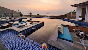 A pool area with blue-tiled flooring, lounge seating, and a view of the sunset. - Casa De Turtle  (Shrivardhan)