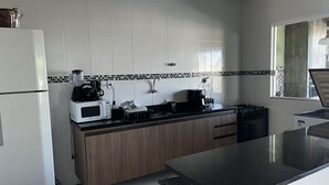 A modern kitchen with white cabinets, a black countertop, and a window providing natural light. - Casa Familia 4 Quartos Condominio Aguas DE Sauipe (Subaúma Entre Rios)