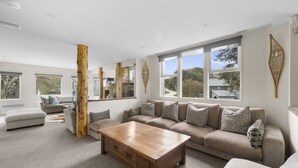 A spacious living room with a large sofa, a wooden coffee table, and a view of the outdoors through large windows.