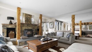 A spacious living room with a stone fireplace, wooden beams, a sofa set, and a coffee table.