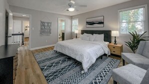 Een slaapkamer met een bed, nachtkastjes, een bureau, een stoel, een plafondventilator en een raam.