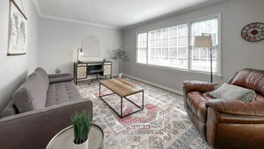 Een woonkamer met een bank, een salontafel, een bureau en een raam met zonwering.