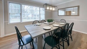 Een eetruimte met een rechthoekige tafel, zes stoelen, een kroonluchter en een grote spiegel aan de muur.