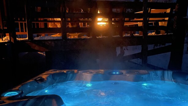 Jacuzzi con dos botellas de cerveza, rodeado por una terraza de madera y árboles.