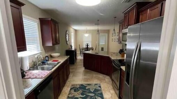 A narrow kitchen with dark wooden cabinets, a stainless steel refrigerator, and a tiled floor.