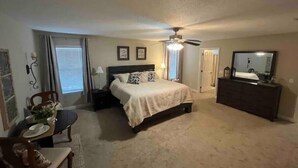 A bedroom with a bed, bedside tables, a ceiling fan, a dresser, a mirror, and a window with curtains.