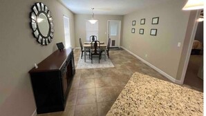 A dining area with a table and chairs, a wall-mounted mirror, and a rug.