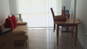 Un salon moderne avec un canapé beige, une table à manger en bois et une fenêtre équipée de stores.