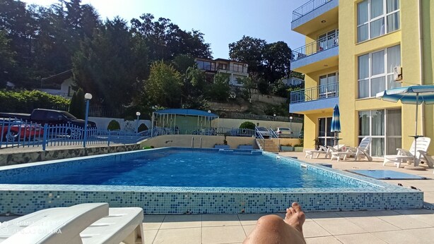 Une piscine dont les bords sont recouverts de carreaux, entourée d’une clôture bleue et située à côté d’un immeuble doté de balcons.