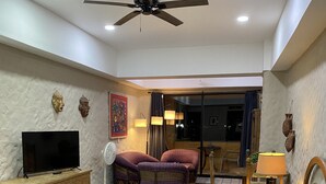 Une chambre d’hôtel avec un lit, une télévision, un ventilateur de plafond et une fenêtre avec des rideaux.