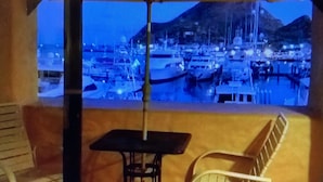 Un balcon avec une table et des chaises, donnant sur une marina où sont amarrés des bateaux, avec une montagne en toile de fond.