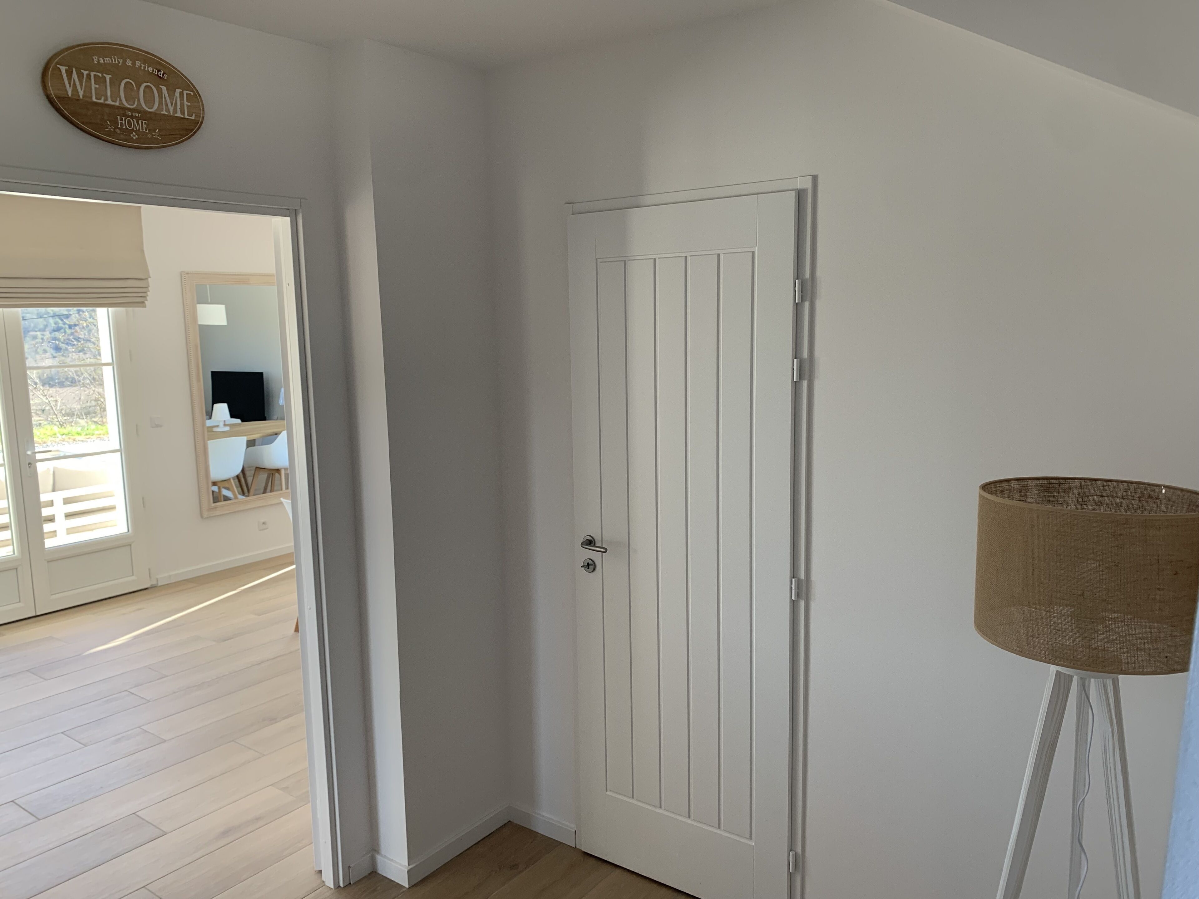 A white door with a vertical panel design, a "Welcome" sign above it, and a floor lamp to the right.