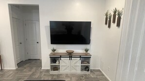 Ett vardagsrum med en platt-TV som är monterad på väggen, ett träbord med dekorativa föremål och två svarta pallar.