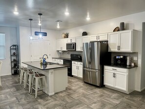 Een moderne keuken met witte kasten, roestvrijstalen apparatuur en een centraal kookeiland met barstoelen.