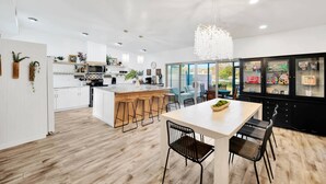A modern kitchen with white cabinets, a central island with stools, and a dining area with a white table and black chairs. - 2 Homes! - 4 Mn To Madeira Bch - Hottub - Htd Pool (Madeira Beach)
