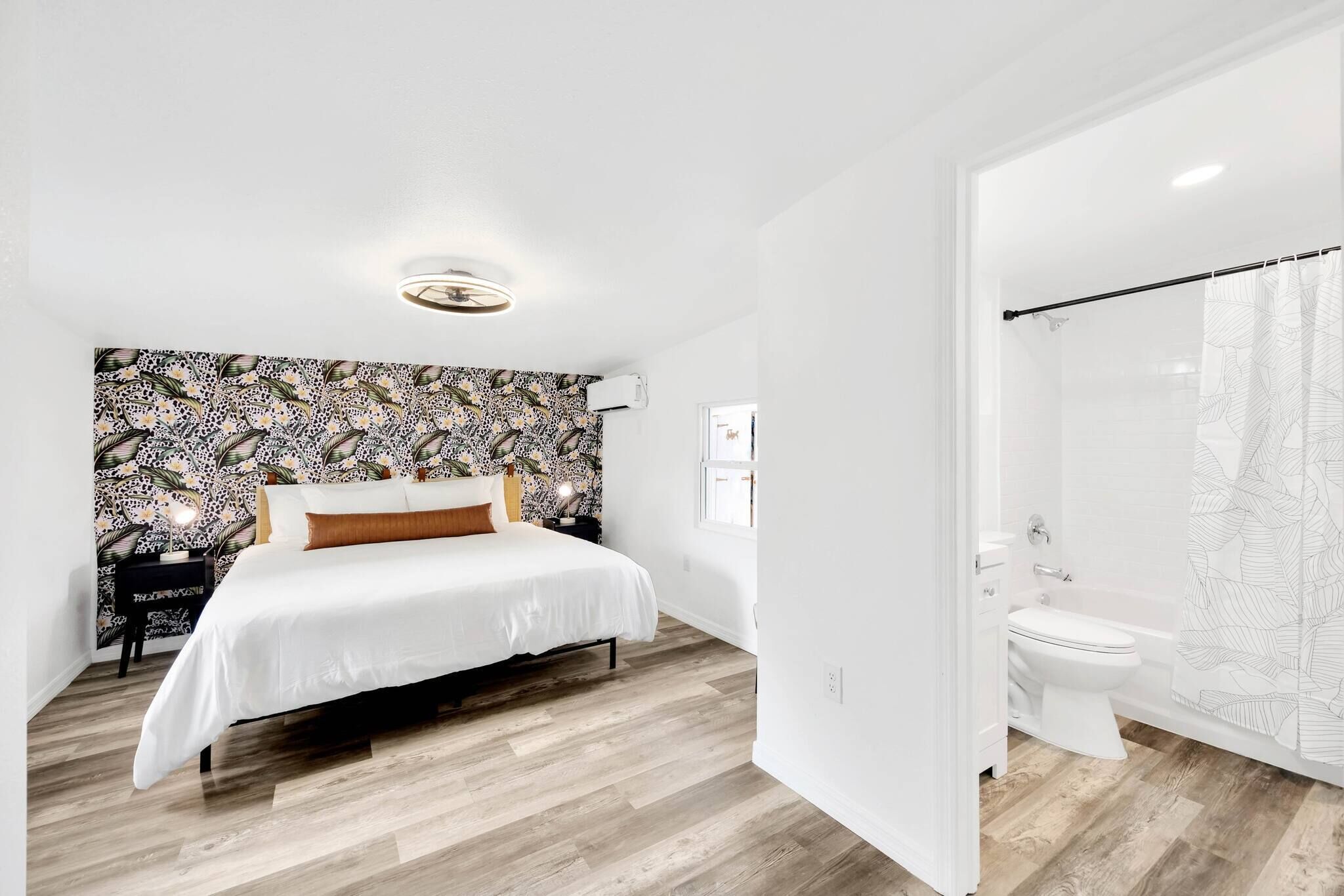 Un dormitorio moderno con una cama grande, un papel pintado decorativo y un baño separado con ducha e inodoro.