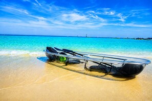 Un kayak sobre una playa arenosa, con agua azul cristalina y un muelle distante.