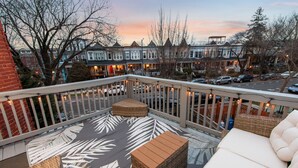 A balcony with wicker furniture, a patterned floor, and a view of residential buildings. - Capitol Hill Retreat | Sleeps 10 | 4BR/3.5BA (Washington)