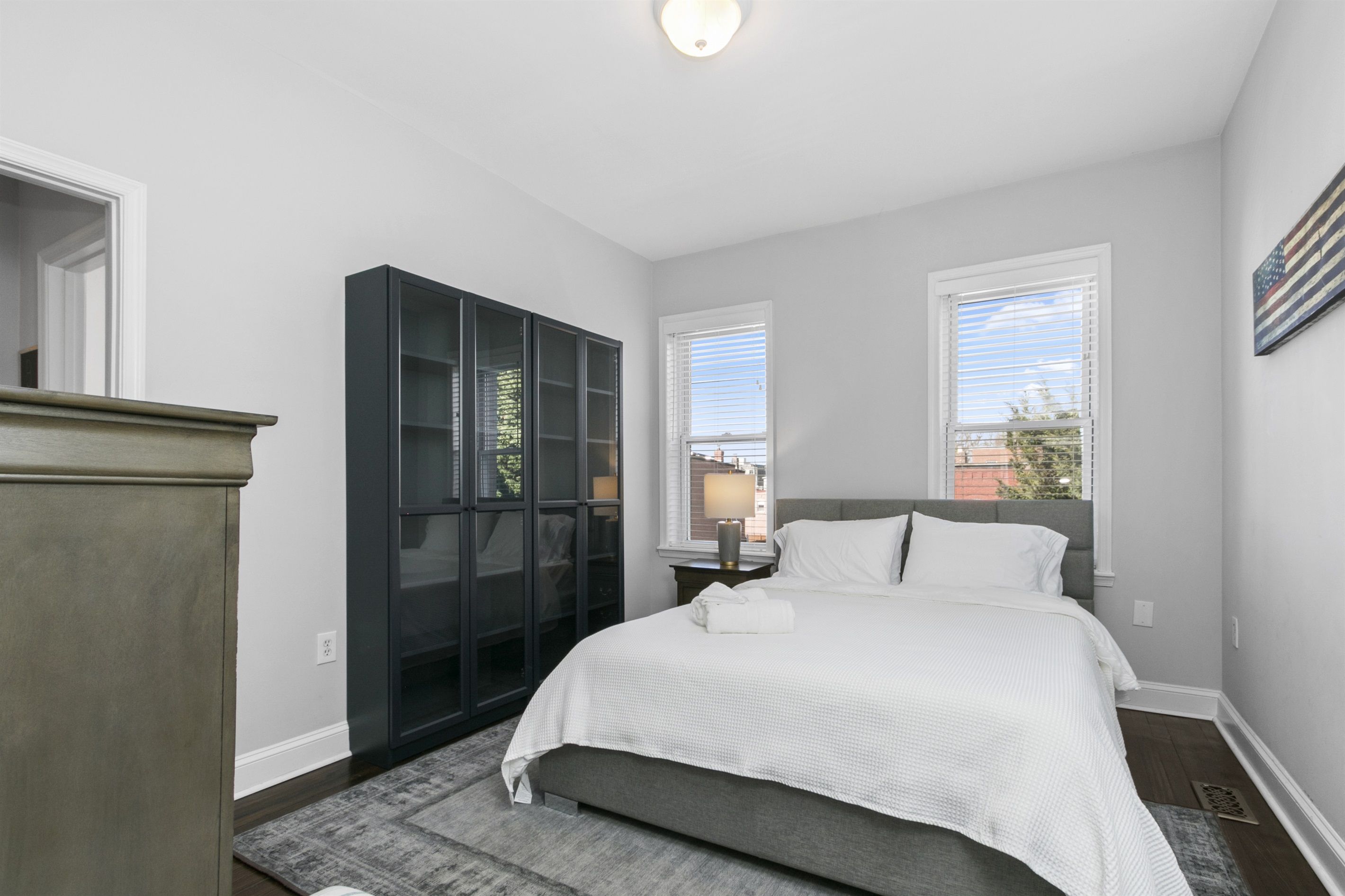 A bedroom with a bed, a wardrobe, and two windows.
