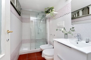 Une salle de bain avec une douche à parois de verre, un lavabo blanc avec un miroir et deux toilettes.