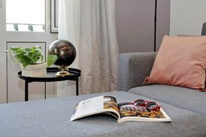 A room with a grey sofa, a small side table with a globe and a plant, and an open magazine.