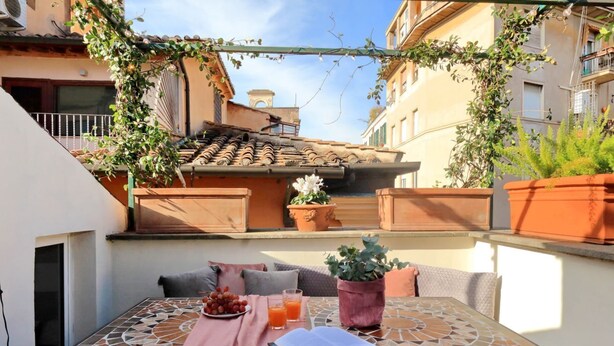 An outdoor patio with a table, cushions, a book, a plate of grapes, and a glass of orange juice. - Campo de Fiori - Rome, nice apartment with terrace for 6 people (Roma)