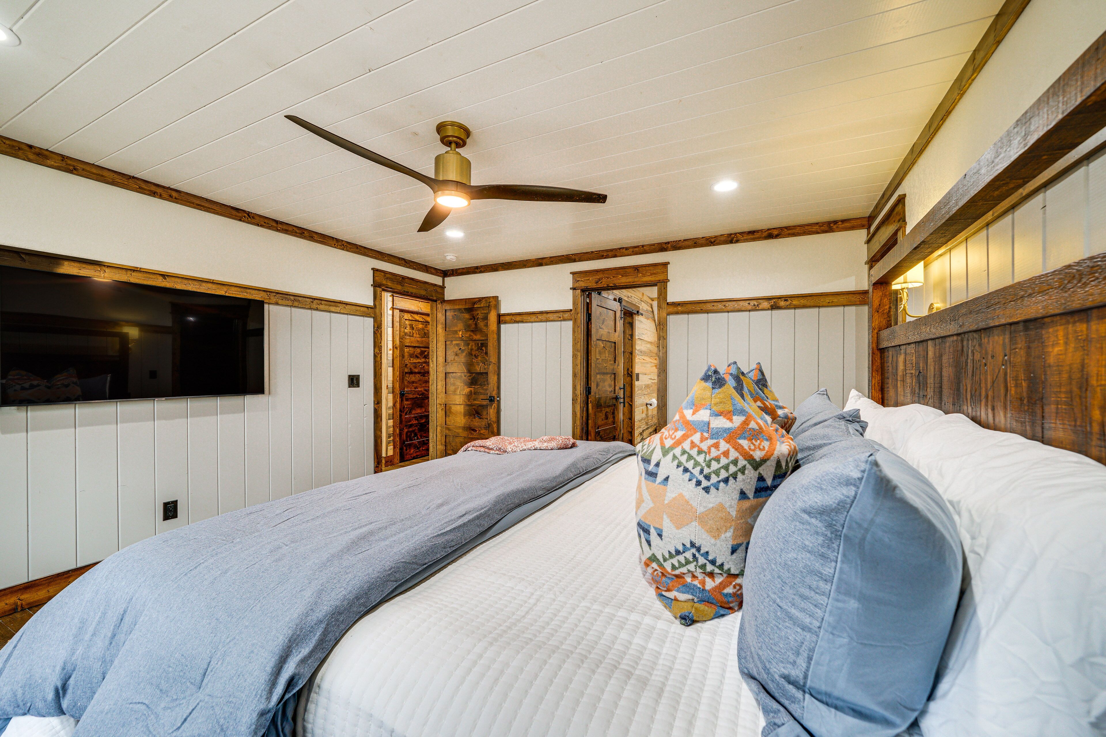 A bedroom with two beds, wooden beams, a ceiling fan, and a TV mounted on the wall.