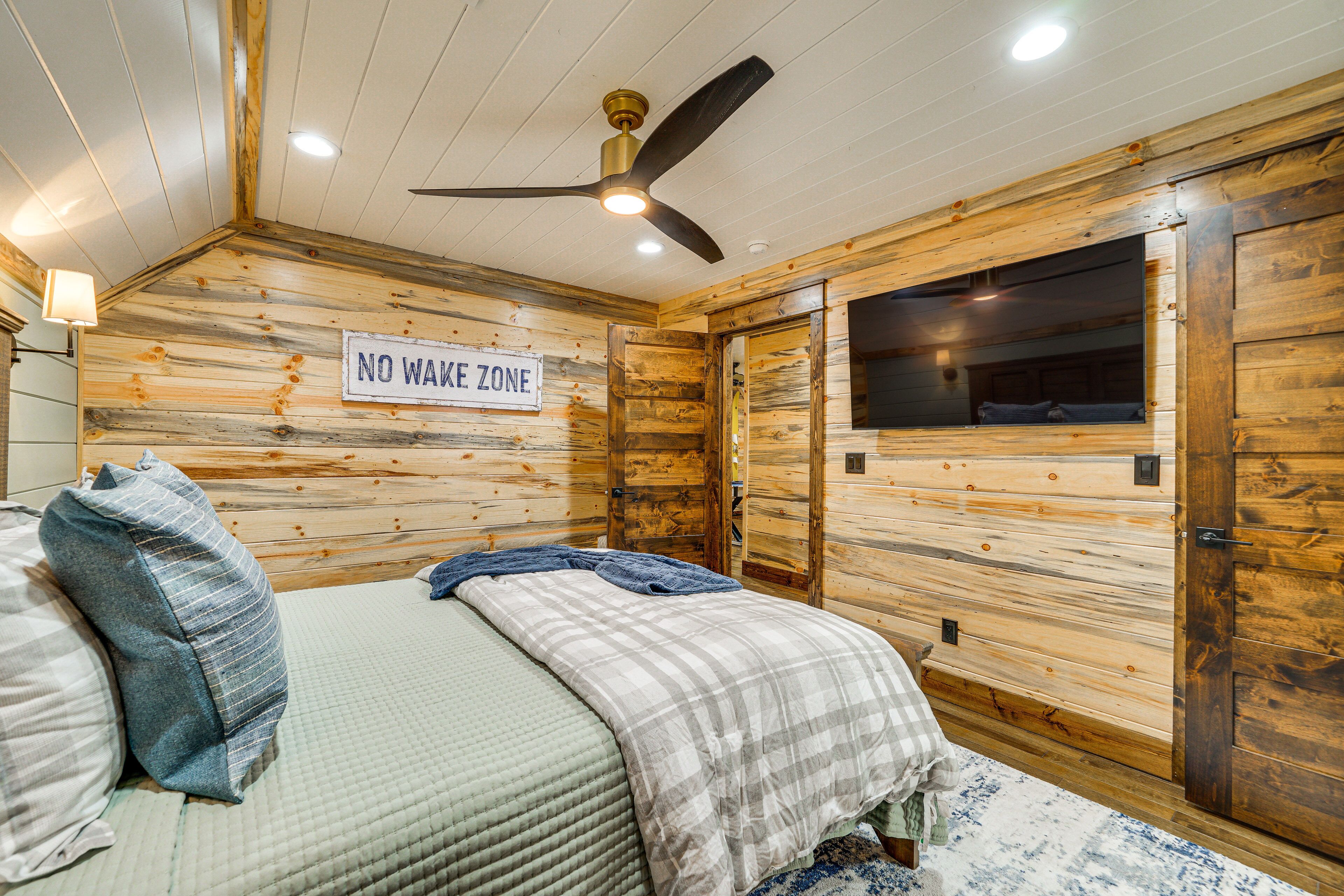 A wooden cabin room with a bed, a ceiling fan, and a 'NO WAKE ZONE' sign.