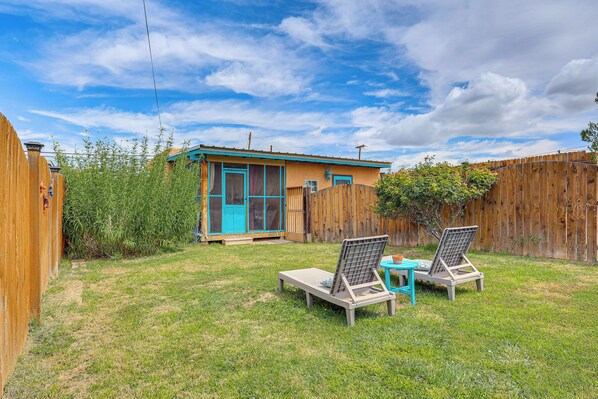 A backyard with a wooden fence, a small house with a blue door, and two lounge chairs. - New Mexico Cottage: Private Yard & Hot Tub (Truth or Consequences)
