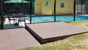 A covered outdoor area with a pool, a patio with chairs, and a yellow building with a mural. - Tropical Pool & Spa Home, 3/2, Near Disney, Universal, Sea World, Beaches (Altamonte Springs)
