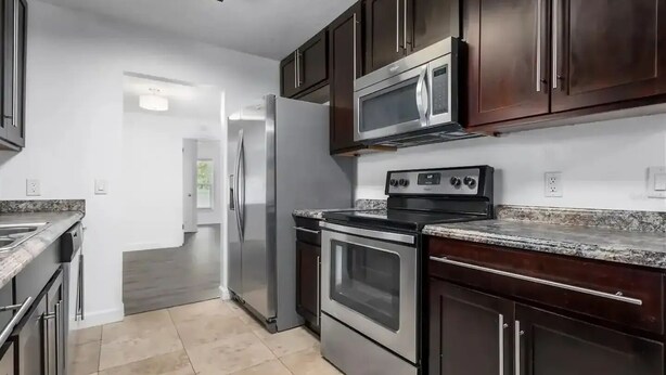 A modern kitchen with stainless steel appliances, dark wooden cabinets, and a granite countertop. - Tropical Pool & Spa Home, 3/2, Near Disney, Universal, Sea World, Beaches (Altamonte Springs)