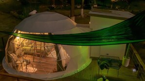 A geodesic dome structure with a hammock, a small table, and a chair outside.