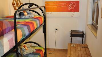 A dormitory room with bunk beds, a small wooden table, and a wall-mounted artwork.