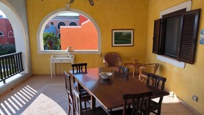 A dining area with a wooden table and chairs, a small white table, and a window with a view of buildings. - BORGO SAN BASILIO APPARTAMENTO PENELOPE-CON PISCINA E ANIMAZIONE DIURNA E SERALE (Pisticci)