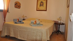 A neatly made bed with striped pillows and a blanket, a small table with a lamp, and a framed picture on the wall. - BORGO SAN BASILIO APPARTAMENTO PENELOPE-CON PISCINA E ANIMAZIONE DIURNA E SERALE (Pisticci)