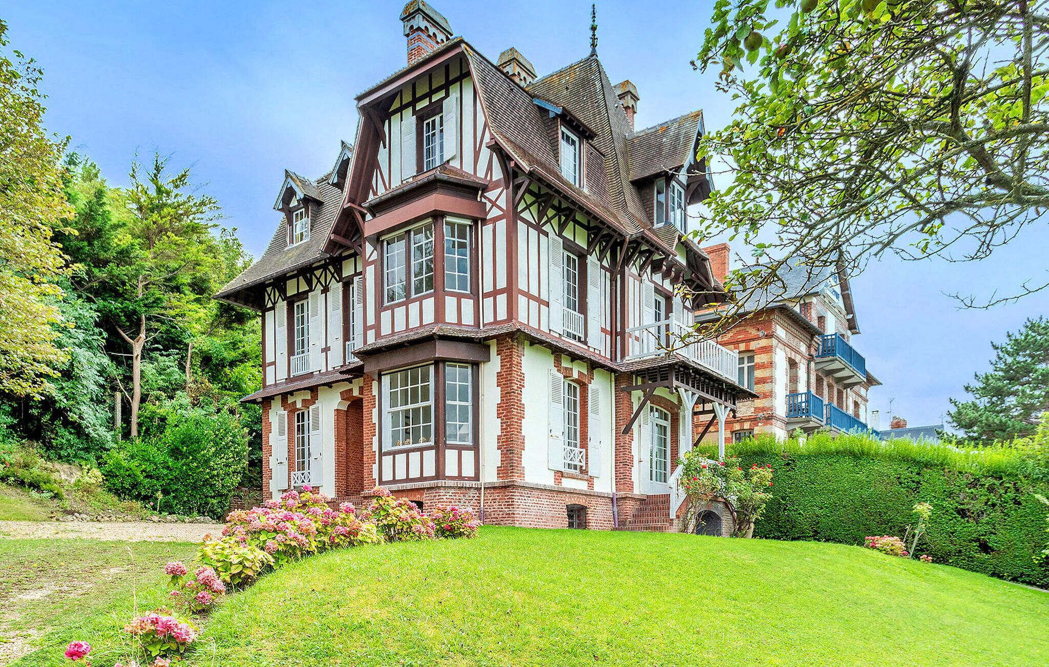 A large, multi-story Tudor-style house with a well-maintained garden and hedges.