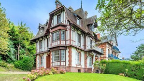 A large, multi-story Tudor-style house with a well-maintained garden and hedges.