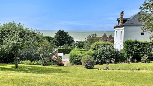 A coastal property with a white building, lush greenery, and a view of the sea.