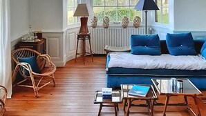 A cozy room with a blue sofa, wicker chairs, a small table with a book, and a window with decorative items.